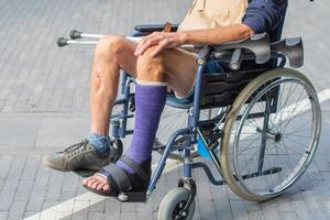 middle-aged Caucasian man sits in a wheelchair with a cast on his broken leg, holding crutches in his hands,concept of two possible modes of movement for person, photo