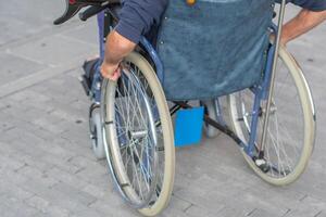unrecognizable man sitting in wheelchair moves along terrace, directing his movement by turning the wheels with his hands,the concept of active living and possible ways of moving for disabled person, photo
