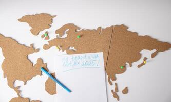 2025 travel wish list written on paper placed on cork board, world map with colored pushpins, on white background, future trip planning concept, photo