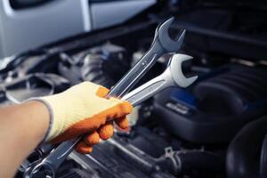 Auto mechanic holding a wrench is repairing a car. Car care and service, professional car mechanic holds wrench to fix parts and repair car engine. photo