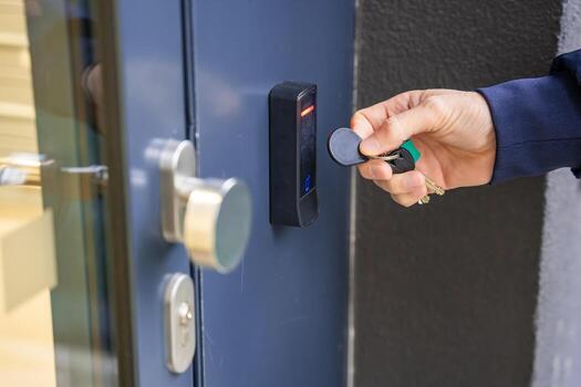Close up view of person using a electric lock key fob to access a building via a reader of entry system mounted on a house wall. High quality photo
