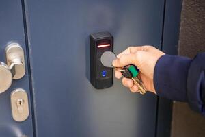 Close up view of person using a electric lock key fob to access a building via a reader of entry system mounted on a house wall. High quality photo