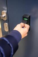 Close up view of person using a electric lock key fob to access a building via a reader of entry system mounted on a house wall. High quality photo