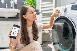 Young woman using mobile phone control via wi-fi and app for washing machine in home. Homesmart and new technology concept photo