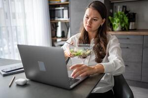 Tired woman eats food ordered at delivery service while sitting in her home office in front of laptop during lunch break. High quality photo