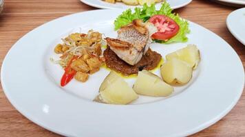Spicy red seasoned fish with boiled potatoes and stir-fried tempe sprouts served on a white plate photo