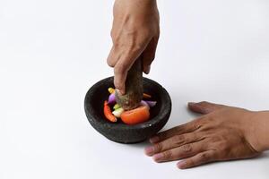 A man uses two hands to make chili sauce in a mortar made of stone photo