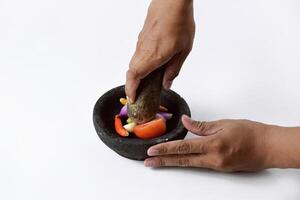 A man uses two hands to make chili sauce in a mortar made of stone photo