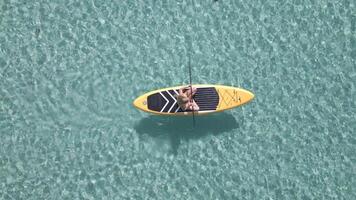 Aerial view of caucasian woman on paddleboard floating in the crystal clear sea video