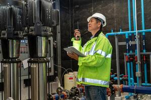 asian man worker in protective uniform and with hardhat using tablet for checking temperature in pipes Factory interior. photo