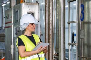 Female industrial engineer wearing a white helmet while standing in a heavy industrial factory photo