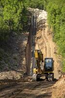 Yellow excavator against the background of a trench with polypropylene pipes. photo