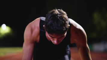 Strong Young Man Starting a Race From Track Starting Blocks Position on a Dark Stadium in the Evening. Cinematic Portrait of a Fit Male Sprint Runner Participating in a Competition video