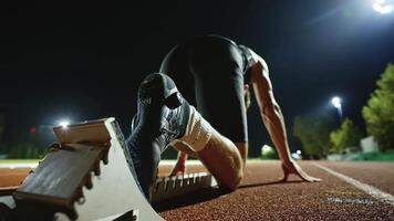Strong Young Man Starting a Race From Track Starting Blocks Position on a Dark Stadium in the Evening. Cinematic Portrait of a Fit Male Sprint Runner Participating in a Competition video