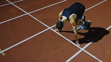 Strong Young Man Starting a Race From Track Starting Blocks Position on a Dark Stadium in the Evening. Cinematic Portrait of a Fit Male Sprint Runner Participating in a Competition video