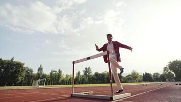 Businessman jumping a hurdle while running on the athletics racing track video