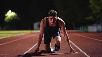 Strong Young Man Starting a Race From Track Starting Blocks Position on a Dark Stadium in the Evening. Cinematic Portrait of a Fit Male Sprint Runner Participating in a Competition video