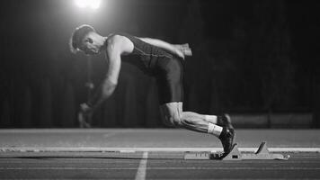 Strong Young Man Starting a Race From Track Starting Blocks Position on a Dark Stadium in the Evening. Cinematic Portrait of a Fit Male Sprint Runner Participating in a Competition video