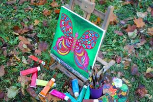 Easel with paints and painting on canvas in autumn park photo