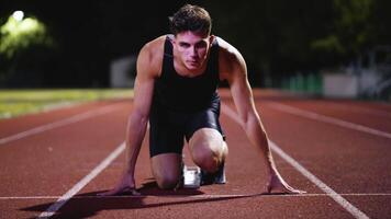 Strong Young Man Starting a Race From Track Starting Blocks Position on a Dark Stadium in the Evening. Cinematic Portrait of a Fit Male Sprint Runner Participating in a Competition video