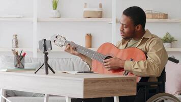 African American man with a joyful expression plays an acoustic guitar while sitting at a desk in his cozy home. Natural light fills the room, creating an inviting atmosphere. video