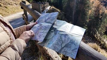 A Caucasian woman in a beige jacket holds a map on a forest trail, symbolizing exploration and adventure video