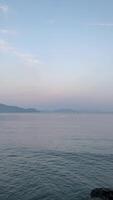 View of gentle waves lapping the shore with fisherman with the boat in the distance. Calm and misty dawn over the tranquil sea at Ulee Lheue beach in Banda Aceh, Indonesia. video