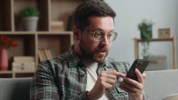 At home concentrated shocked confused puzzled amazed wonder gadget addict man guy male using mobile phone app smartphone social media receive message bad news browsing internet service relax on couch video