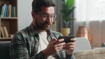 Caucasian man male guy user gamer at home game addict browsing mobile phone play app playing smartphone shock emotional entertainment at home couch sofa apartment gaming online internet web fun video