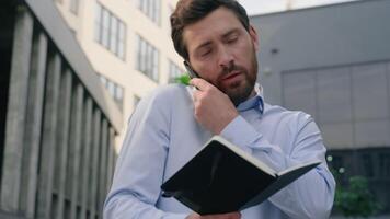 Caucasian businessman adult man business guy male employer entrepreneur real estate agent building city development trader talking mobile phone call writing notes information in notebook negotiation video