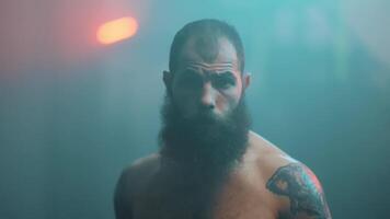 A man with a beard and tattoos standing in front of a light video