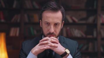 A man in a suit and tie sitting in front of a book shelf video