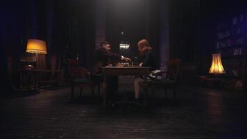 A man and woman sitting at a table in a dark room video