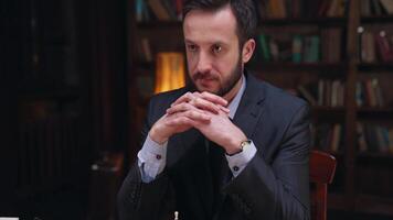 A man in a suit sitting at a table with a chess board video