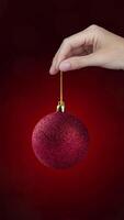 Motion animation with red Christmas ball with yellow 2025 in a hand on red background, vertical banner video