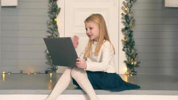 little girl making a call using a laptop. The girl sits on the doorstep of her house and communicates via link holding a laptop on her lap video
