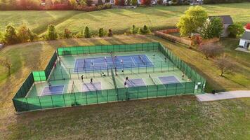 Aerial View of Pickleball Courts in Use, Drone shot of outdoor pickleball courts with players engaged in games, surrounded by green fencing and open fields. video