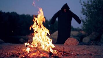 Monk pray at the campfire. Man in a cassock performs around fire video
