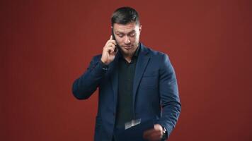 Smiling man talking on the phone. Office worker in dark blue suit with a folder in his hand isolated in studio. Portrait of a happy businessman with a mobile phone. video