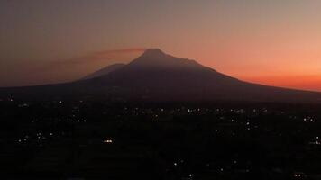 The panorama towards the morning of the active volcano from a distance is still a silhouette with a thin light. 4k aerial footage of Mount Merapi from a distance when it was still dark before sunrise. video
