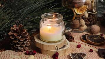 Vanilla candle burns on a wooden platform with a Christmas background of pine branches and cones cinnamon sticks dried oranges video