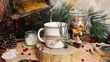 Tea is poured from the transparent teapot into the mug decorated with a pine tree, and there are Christmas decorations in the background Candle cinnamon pine cones Cozy atmosphere video