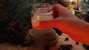 A girl takes the burning candle in her hand and puts it out, on a cozy Christmas background with dried oranges pine branches and cones cinnamon sticks video