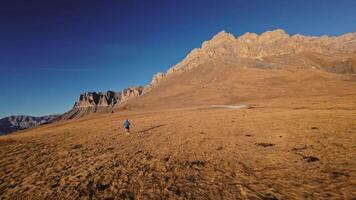 Aerial view of a man in sportswear running fast across fields. A guy exercising outdoors in nature in the mountains covered with snow. View from below near the legs, healthy lifestyle video