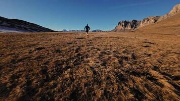 Aerial view of a man in sportswear running fast across fields. A guy exercising outdoors in nature in the mountains covered with snow. View from below near the legs, healthy lifestyle video
