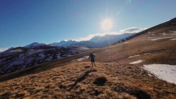 Aerial view of a man in sportswear running fast across fields. A guy exercising outdoors in nature in the mountains covered with snow. View from below near the legs, healthy lifestyle video