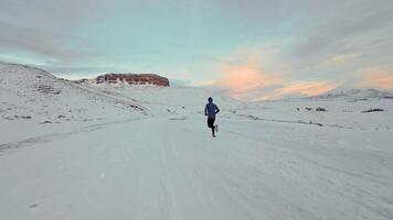 Aerial drone view of young man jogging outdoors with snowy mountains in the background. Healthy running and exercise concept outdoors, high-speed drone fvp shooting, slow motion video