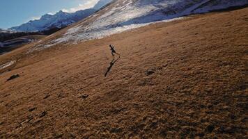 Aerial view of a man in sportswear running fast across fields. A guy exercising outdoors in nature in the mountains covered with snow. View from below near the legs, healthy lifestyle video