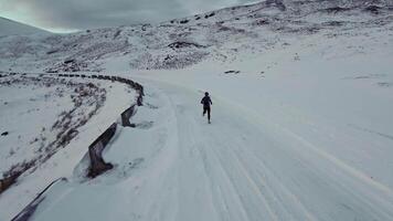Aerial drone view of young man jogging outdoors with snowy mountains in the background. Healthy running and exercise concept outdoors, high-speed drone fvp shooting, slow motion video