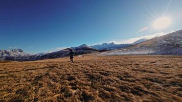 Aerial view of a man in sportswear running fast across fields. A guy exercising outdoors in nature in the mountains covered with snow. View from below near the legs, healthy lifestyle video